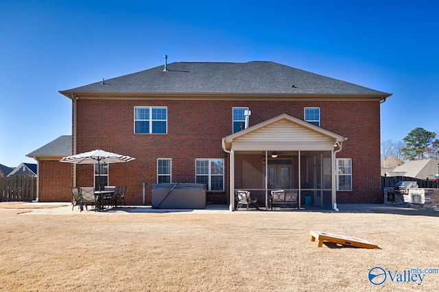 rear view of house with brick siding, a hot tub, a patio, and a sunroom