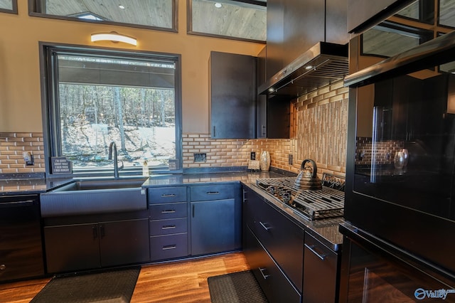 kitchen with dark countertops, light wood-style flooring, backsplash, black appliances, and a sink