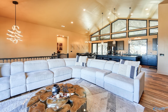 living room with high vaulted ceiling, recessed lighting, an inviting chandelier, and wood finished floors