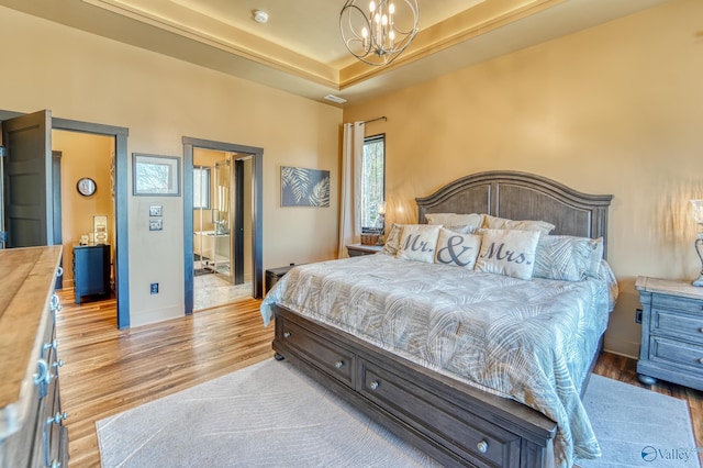 bedroom with a tray ceiling, a notable chandelier, baseboards, and wood finished floors