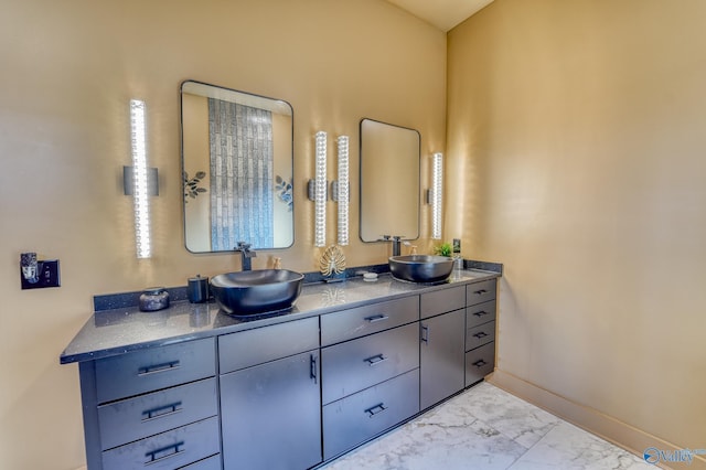 bathroom featuring marble finish floor, double vanity, a sink, and baseboards