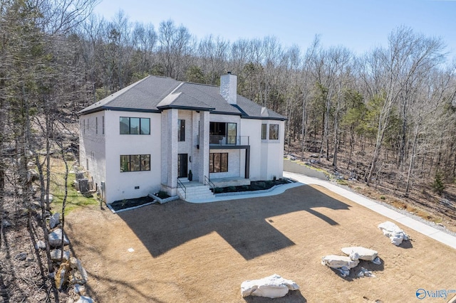 view of front of house featuring a balcony, a chimney, a wooded view, and roof with shingles