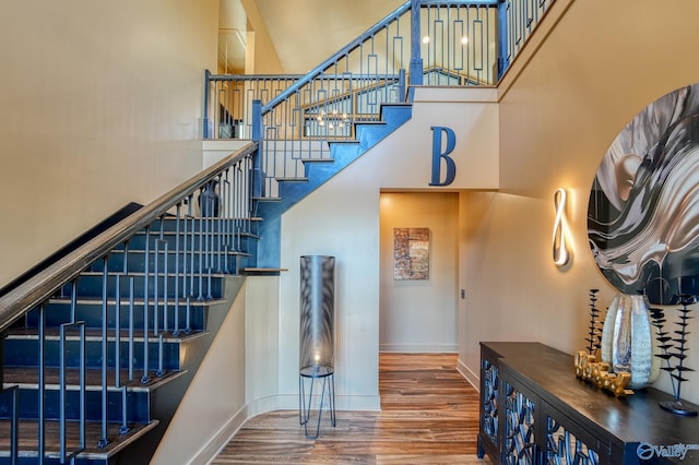 stairway featuring wood finished floors, a towering ceiling, and baseboards