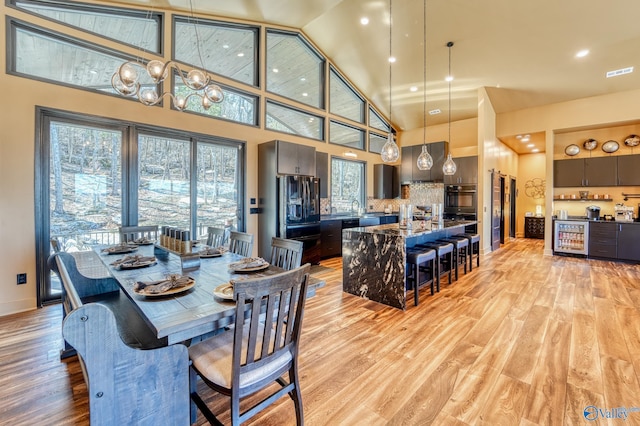 dining room with high vaulted ceiling, visible vents, indoor bar, and light wood finished floors