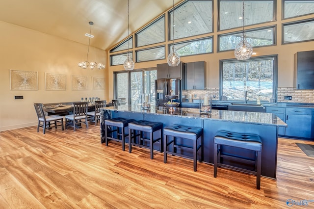 kitchen with stainless steel fridge, light wood-style flooring, a breakfast bar area, dark stone countertops, and a sink