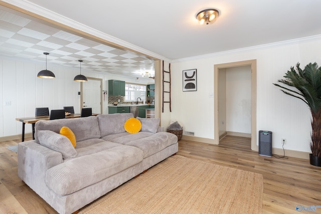 living area featuring ornamental molding, baseboards, visible vents, and light wood finished floors