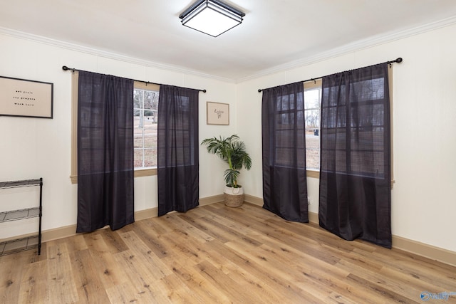 empty room featuring light wood-type flooring, baseboards, and crown molding