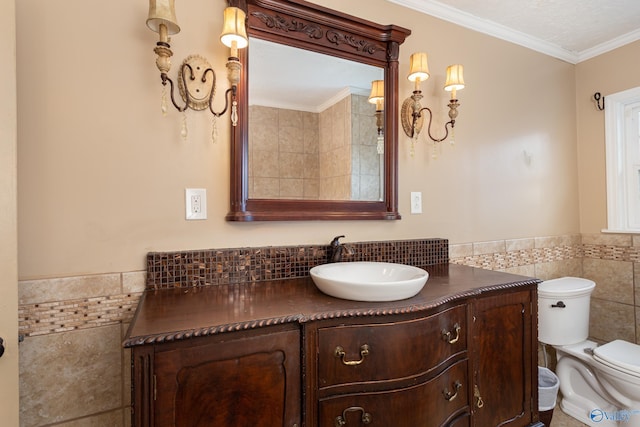 bathroom featuring a wainscoted wall, crown molding, tile walls, toilet, and vanity