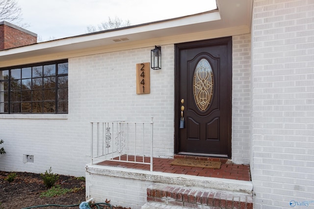 view of exterior entry featuring crawl space and brick siding