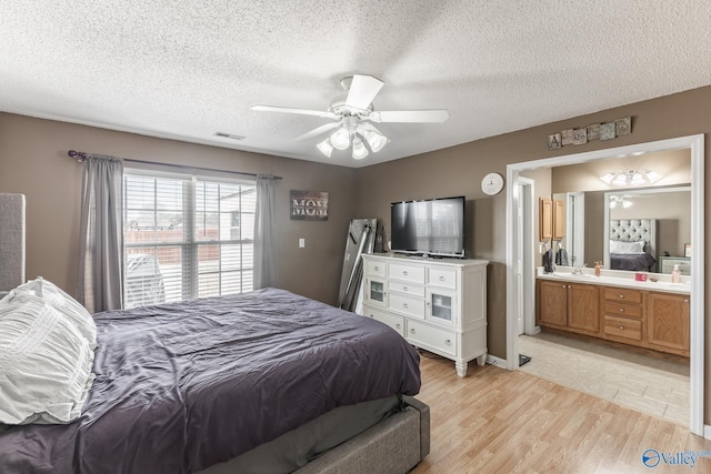 bedroom featuring sink, ensuite bath, light hardwood / wood-style flooring, ceiling fan, and a textured ceiling