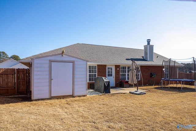 rear view of property with a trampoline, a yard, a patio, and a storage unit