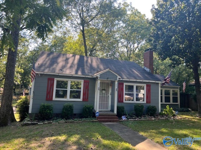 bungalow-style house with a shingled roof, a chimney, and a front yard