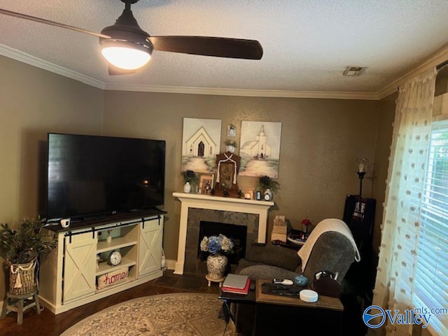 living room with ceiling fan, ornamental molding, a tiled fireplace, a textured ceiling, and dark tile patterned floors