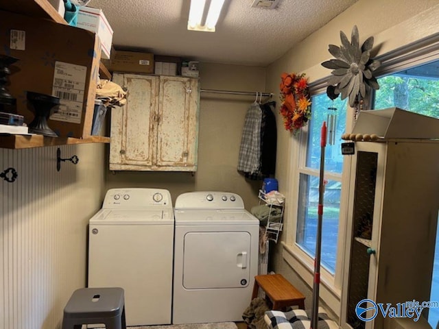 laundry area with washer and dryer, a textured ceiling, and cabinets