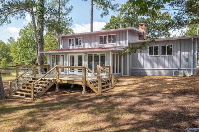 rear view of house with board and batten siding, stairs, a deck, a chimney, and french doors