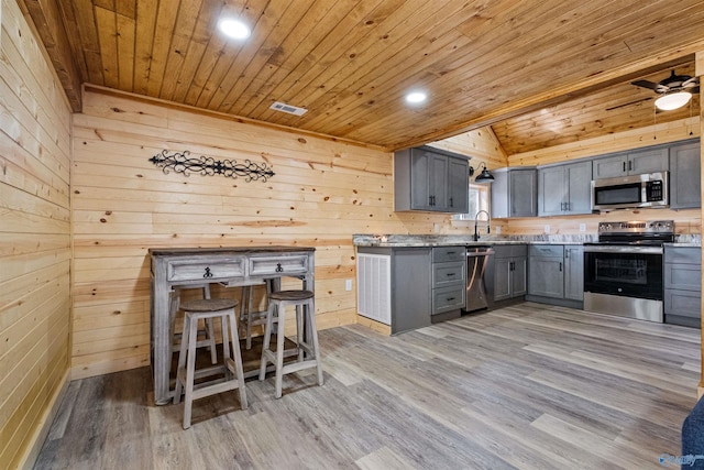 kitchen with lofted ceiling, wood ceiling, a sink, appliances with stainless steel finishes, and gray cabinetry