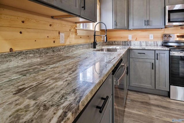 kitchen featuring a sink, gray cabinets, light stone counters, appliances with stainless steel finishes, and wood finished floors