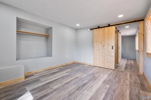 interior space with baseboards, a barn door, wood finished floors, and recessed lighting