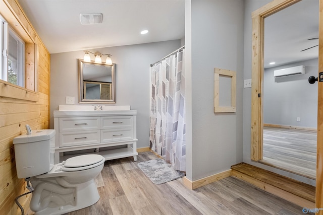 bathroom with baseboards, toilet, an AC wall unit, wood finished floors, and vanity