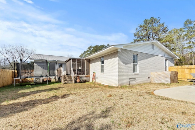 rear view of house featuring a trampoline, a patio area, a sunroom, and a lawn