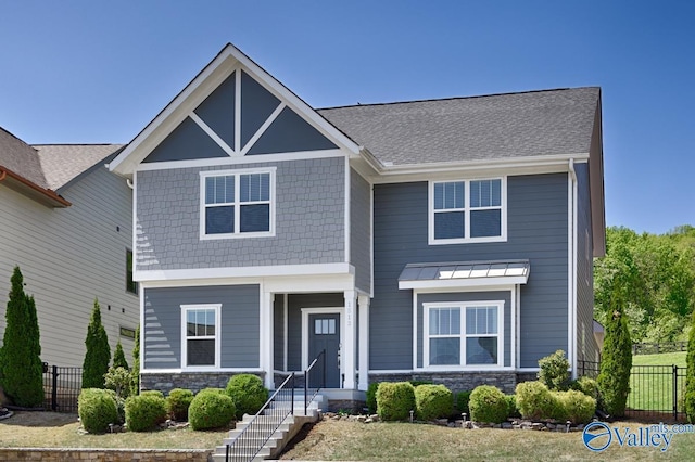 craftsman-style home with fence, a shingled roof, and stone siding