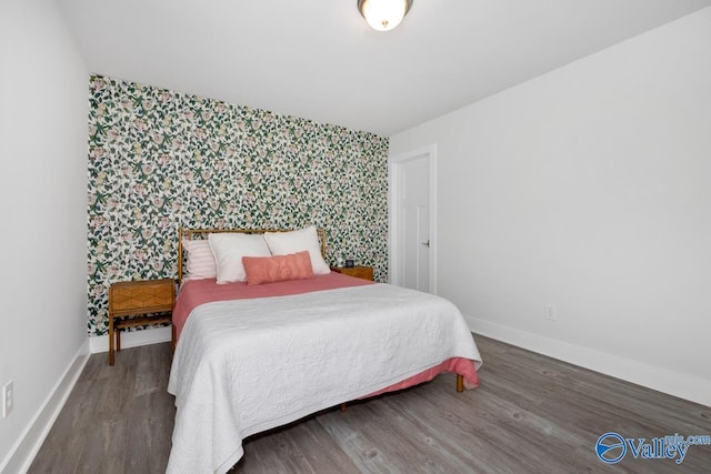 bedroom featuring baseboards, wallpapered walls, wood finished floors, and an accent wall