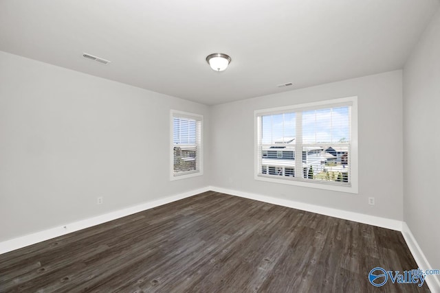 spare room featuring dark wood-style floors, visible vents, and baseboards