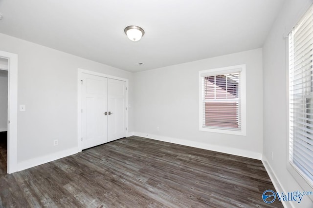 unfurnished bedroom with baseboards, wood finished floors, multiple windows, and a closet