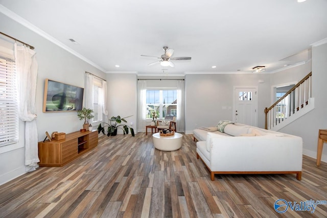 living room featuring crown molding, a ceiling fan, visible vents, baseboards, and wood finished floors