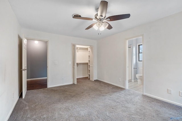 unfurnished bedroom with light carpet, a walk in closet, a closet, and ceiling fan