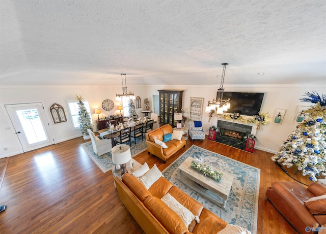 living room featuring vaulted ceiling, wood-type flooring, a textured ceiling, and a notable chandelier