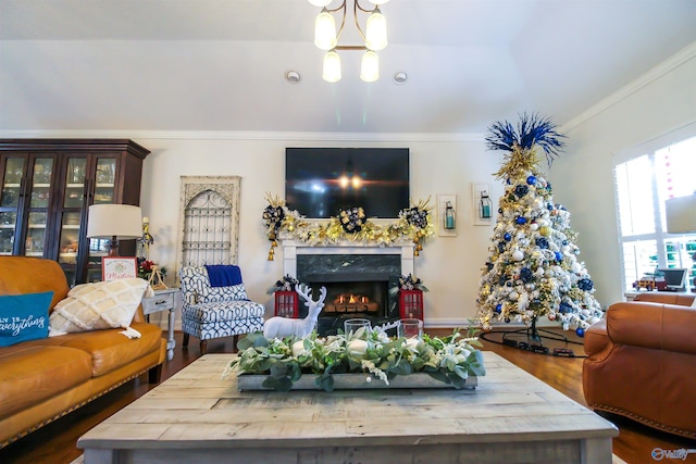 living room featuring an inviting chandelier, a premium fireplace, wood-type flooring, vaulted ceiling, and ornamental molding