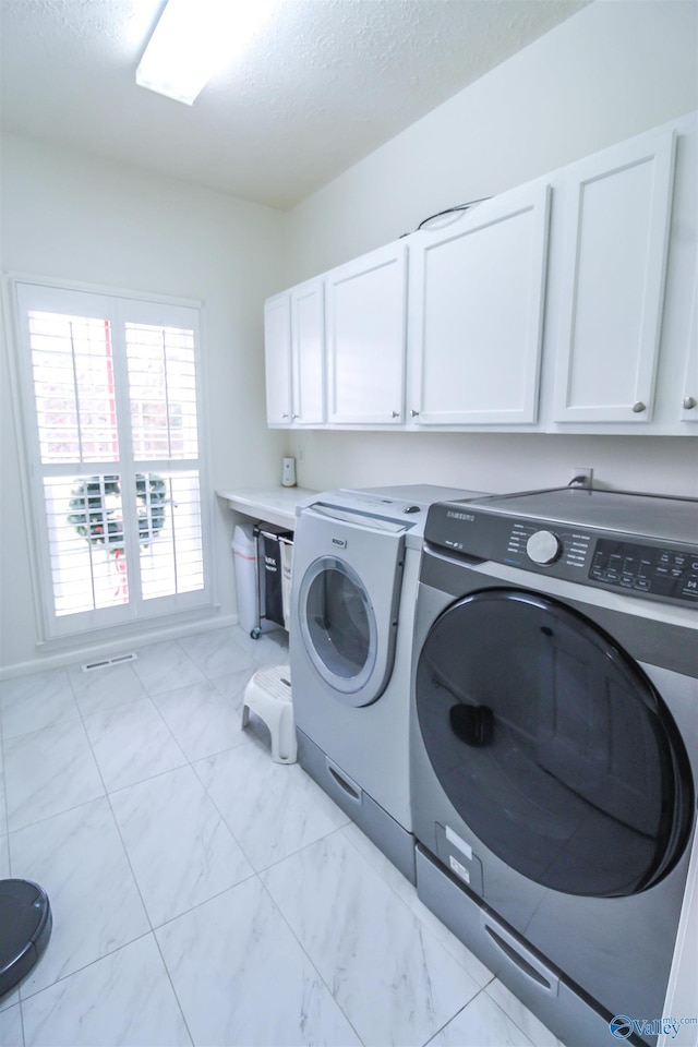 laundry room featuring washing machine and clothes dryer, cabinets, and a textured ceiling