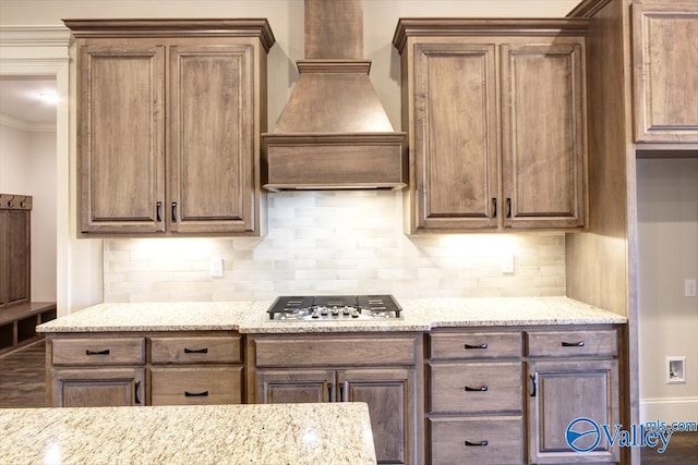 kitchen featuring decorative backsplash, custom exhaust hood, light stone countertops, and stainless steel gas stovetop