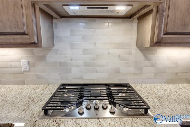 kitchen with light stone countertops, backsplash, exhaust hood, and stainless steel gas cooktop