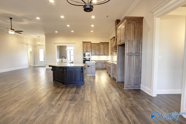 kitchen featuring sink, dark hardwood / wood-style flooring, ornamental molding, ceiling fan, and a center island with sink