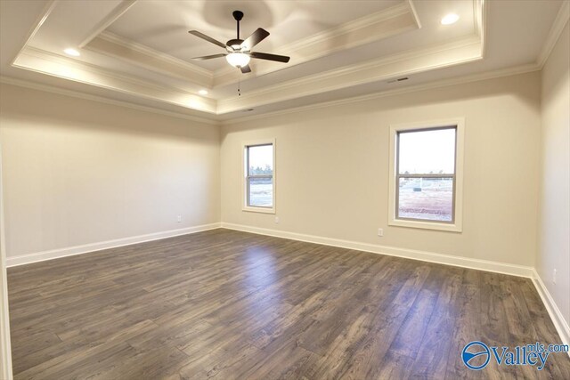 empty room with a tray ceiling, dark wood-type flooring, ornamental molding, and ceiling fan