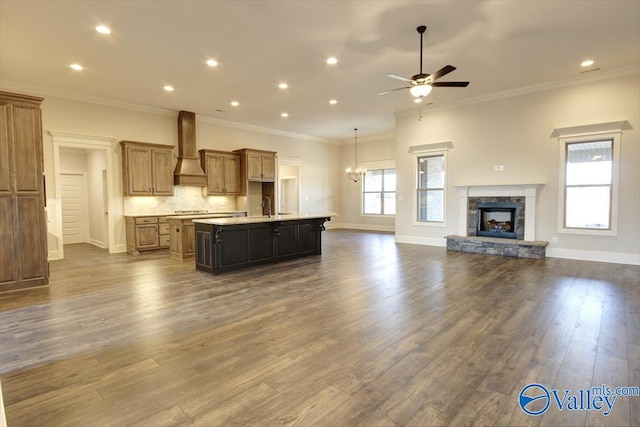 kitchen with hardwood / wood-style floors, a fireplace, custom range hood, an island with sink, and ceiling fan with notable chandelier