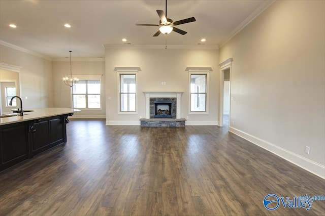 unfurnished living room featuring ceiling fan with notable chandelier, a fireplace, sink, dark hardwood / wood-style flooring, and ornamental molding