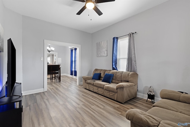 living area featuring light wood-type flooring, baseboards, and ceiling fan with notable chandelier