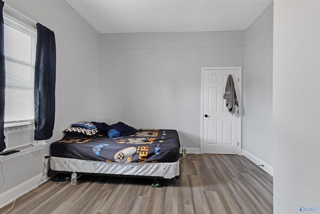 bedroom with cooling unit, baseboards, and wood finished floors