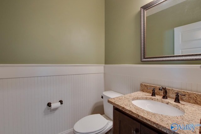 bathroom with toilet, vanity, and wainscoting