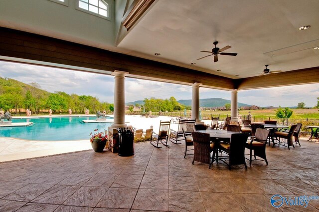 view of patio / terrace featuring a community pool, a mountain view, outdoor dining area, and a ceiling fan