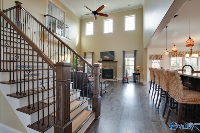 stairway featuring crown molding, hardwood / wood-style floors, a ceiling fan, a stone fireplace, and baseboards