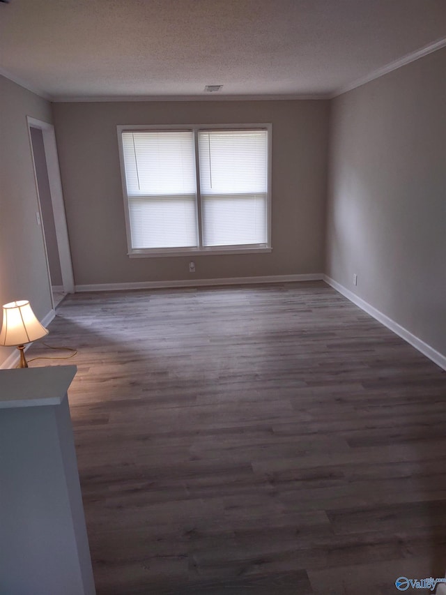empty room featuring a textured ceiling, ornamental molding, visible vents, wood finished floors, and baseboards