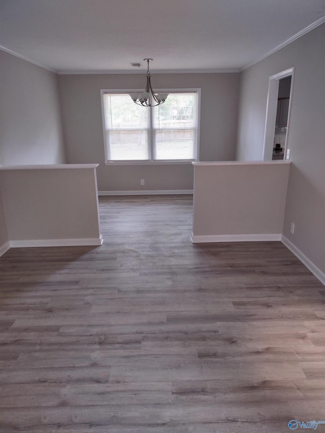 empty room featuring a chandelier, crown molding, wood finished floors, and baseboards