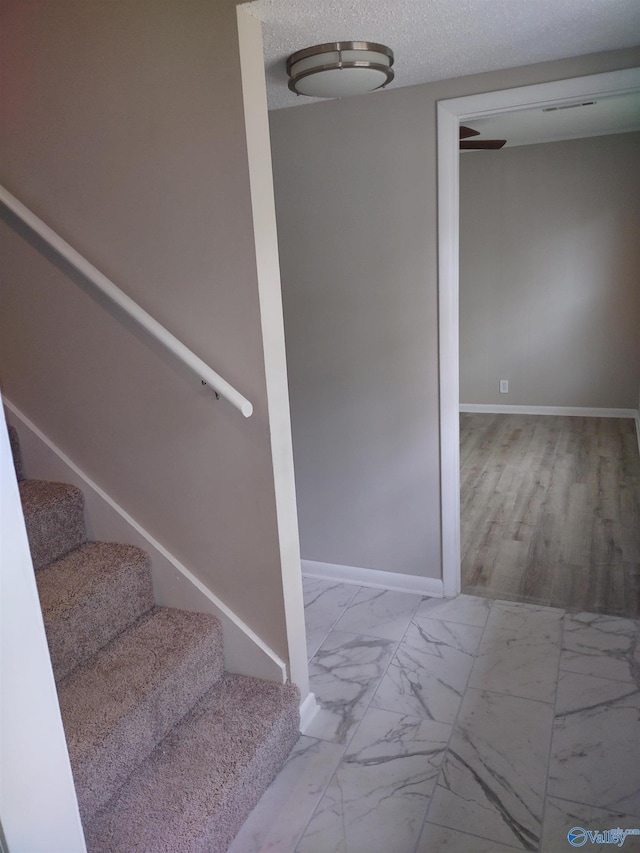 staircase with a textured ceiling, marble finish floor, and baseboards