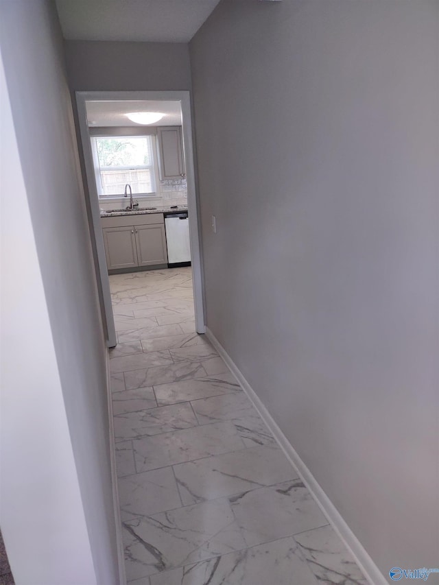 corridor featuring baseboards, marble finish floor, and a sink