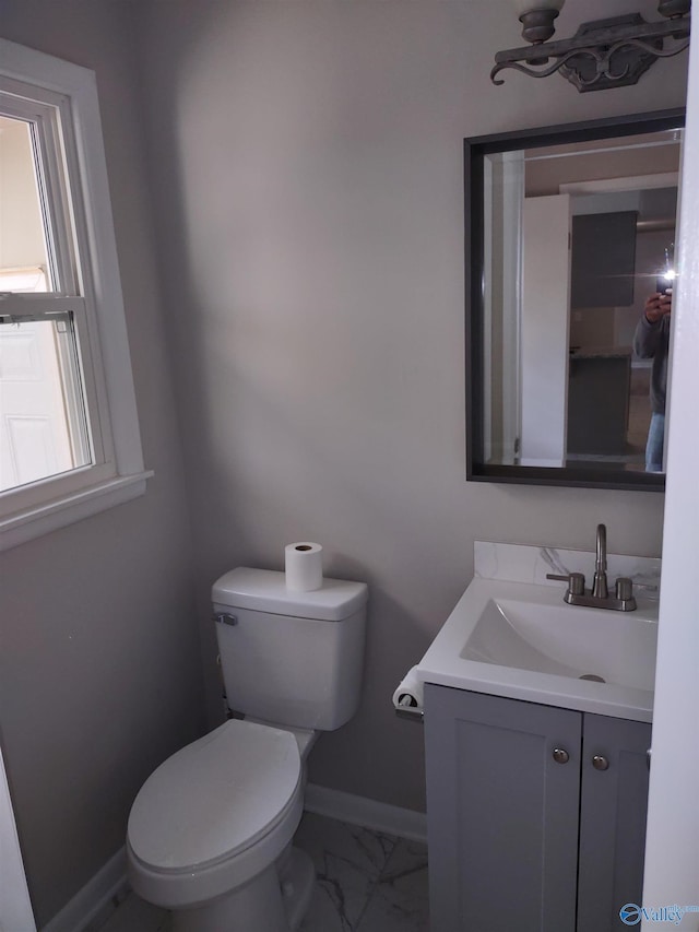 half bath with toilet, marble finish floor, vanity, and baseboards