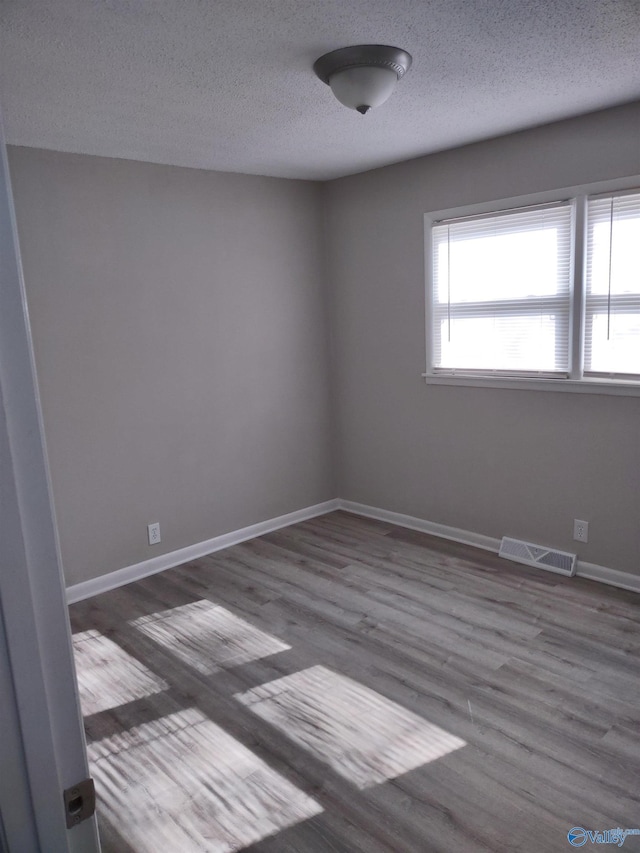 spare room featuring a textured ceiling, wood finished floors, baseboards, and visible vents